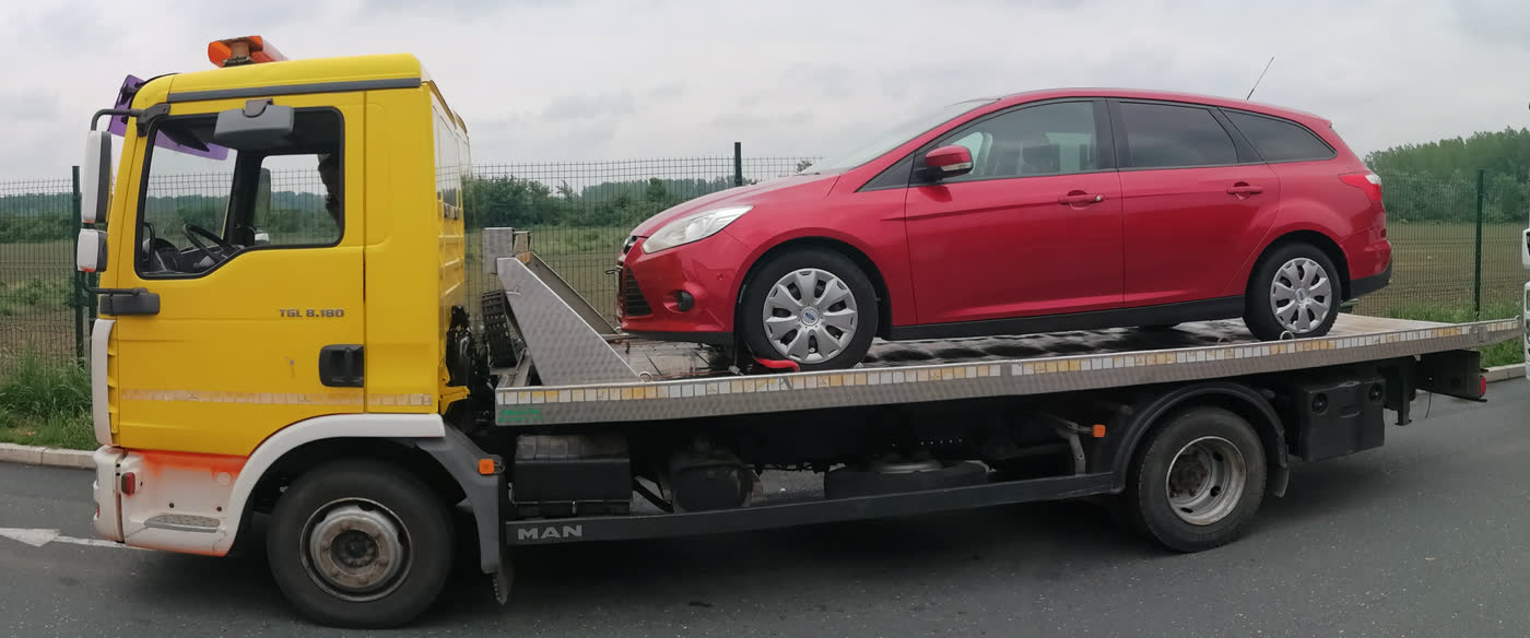 Crveni karavan na platformi žutog šlepera, na odmorištu uz autoput.
