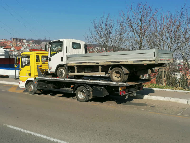 Beli manji kamion sa aluminijumskim sandukom na platformi žutog MAN šlepera.