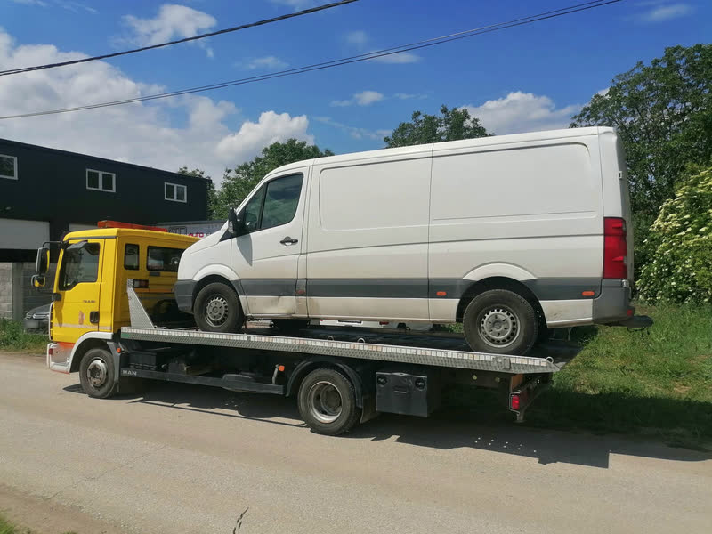 Beli kombi Volkswagen Crafter na platformi žutog šlepera, iz profila.