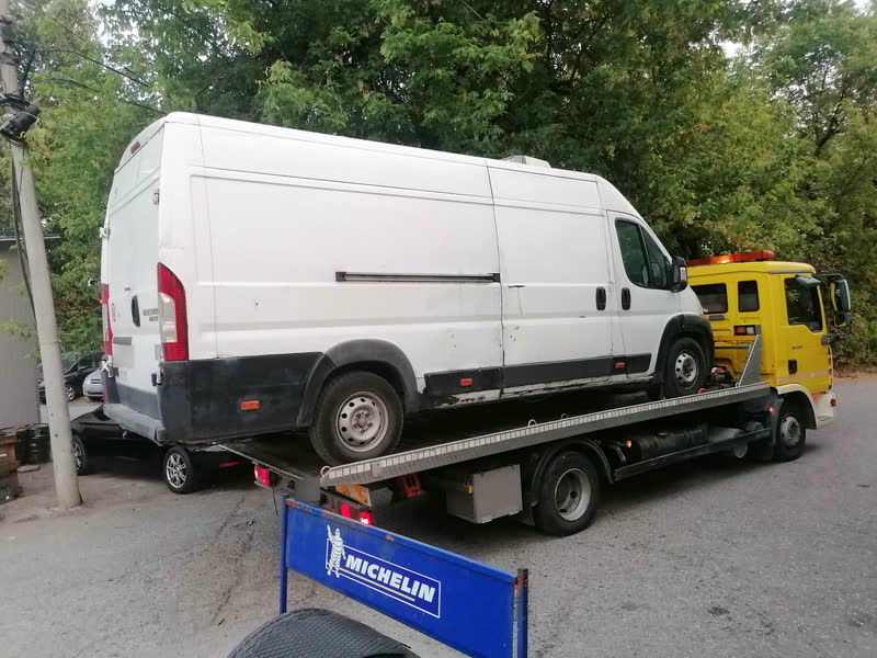 Beli visoki kombi Fiat Ducato na platformi žutog šlepera, snimljen otpozadi.
