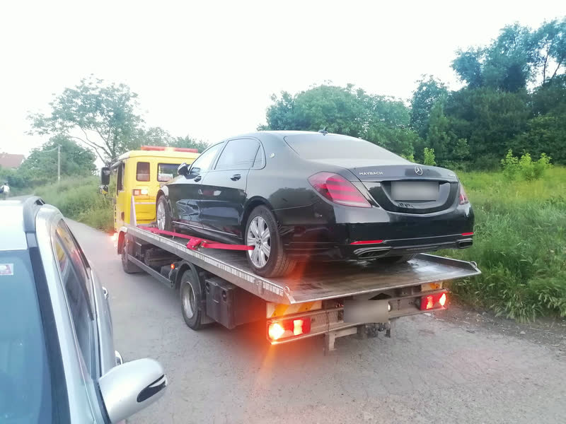 Crni blindirani Mercedes-Maybach vezan crvenim trakama na platformi žutog šlepera, snimljen otpozadi, u sumrak.